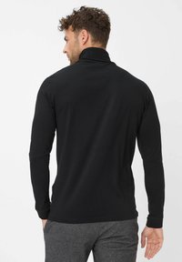 Zwarte polo met lange mouwen en hoge kraag, gemaakt van zachte stof. De achterkant heeft een getailleerd ontwerp en subtiele stikdetails.