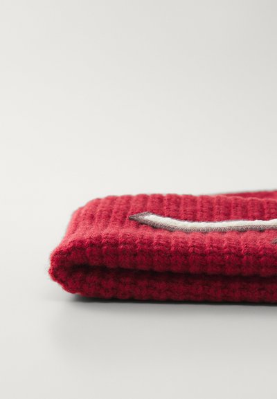 Punane koetud tekk tekstureeritud soonikkudumiga, mille ääres on valge ja hall aktsentvorm. Pehme, kokku volditud esitlus.