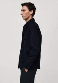 Donkerblauwe shirtjack in een gestructureerde stof, met een knoopsluiting aan de voorkant, twee borstzakken en een klassieke kraag. Glad afgewerkt.