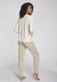 Crème kleurige longsleeve top gecombineerd met lichtgroene pyjamabroek met een verspreid patroon van rode kerststokken, en elastische boorden en tailleband.