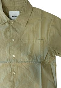 Camicia beige a button-up realizzata in materiale leggero, con colletto a punta, taschino frontale e una sottile texture stropicciata.