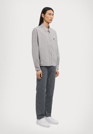 Gray checkered long-sleeve shirt with a pointed collar, button placket, and a small embroidered logo, paired with dark jeans and white sneakers.