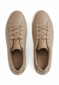 Baskets beige avec une tige en cuir lisse, bout rond, lacets à l'avant et semelle en caoutchouc blanche contrastante. Détails dorés près du talon.