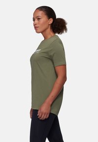 Olivengrøn t-shirt med korte ærmer i blødt materiale, med rund halsudskæring og hvid teksttryk på brystet. Bæres med mørke leggings.