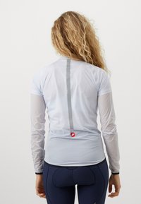Langermet lyseblå sykkeldrakt laget av pustende stoff, med en reflekterende vertikal stripe og logo nederst på ryggen.