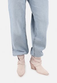 Jean en denim bleu clair associé à des bottines beiges en daim avec des lanières tressées et des talons carrés en bois.