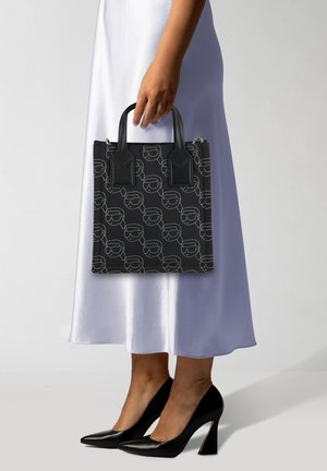 Borsa a tracolla nera con un motivo ripetuto di volti stilizzati, con contorni bianchi a contrasto. Presenta manici corti neri e una forma strutturata.