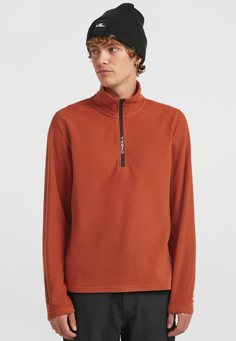 Fleece-pullover i bränd orange med halvdragkedja, med svart dragkedja och "O'Neill"-logotyp på kragen. Långa ärmar, mjuk textur.