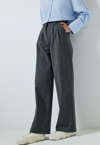 Grijze gestreepte broek met een losse pasvorm, hoge taille, plooien aan de voorkant en een gladde textuur. Gecombineerd met witte sneakers.