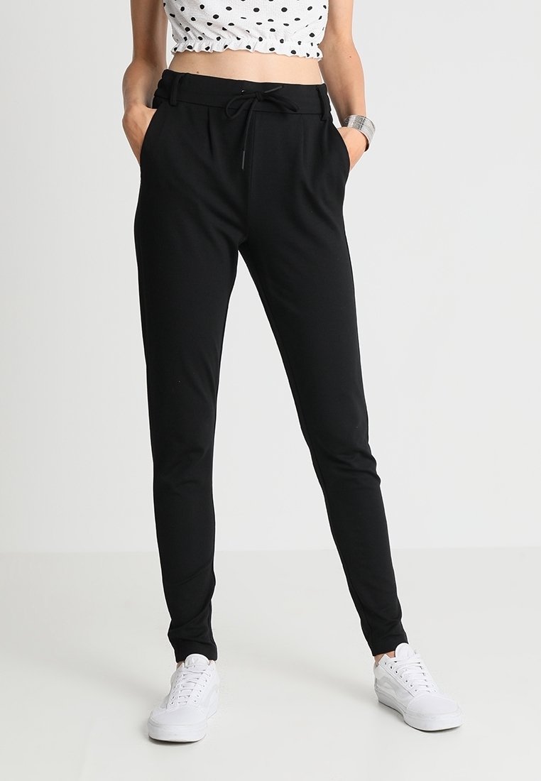 Pantaloni jogger neri con vita regolabile e tasche laterali, realizzati in un tessuto morbido, abbinati a sneakers bianche e a un crop top a pois.