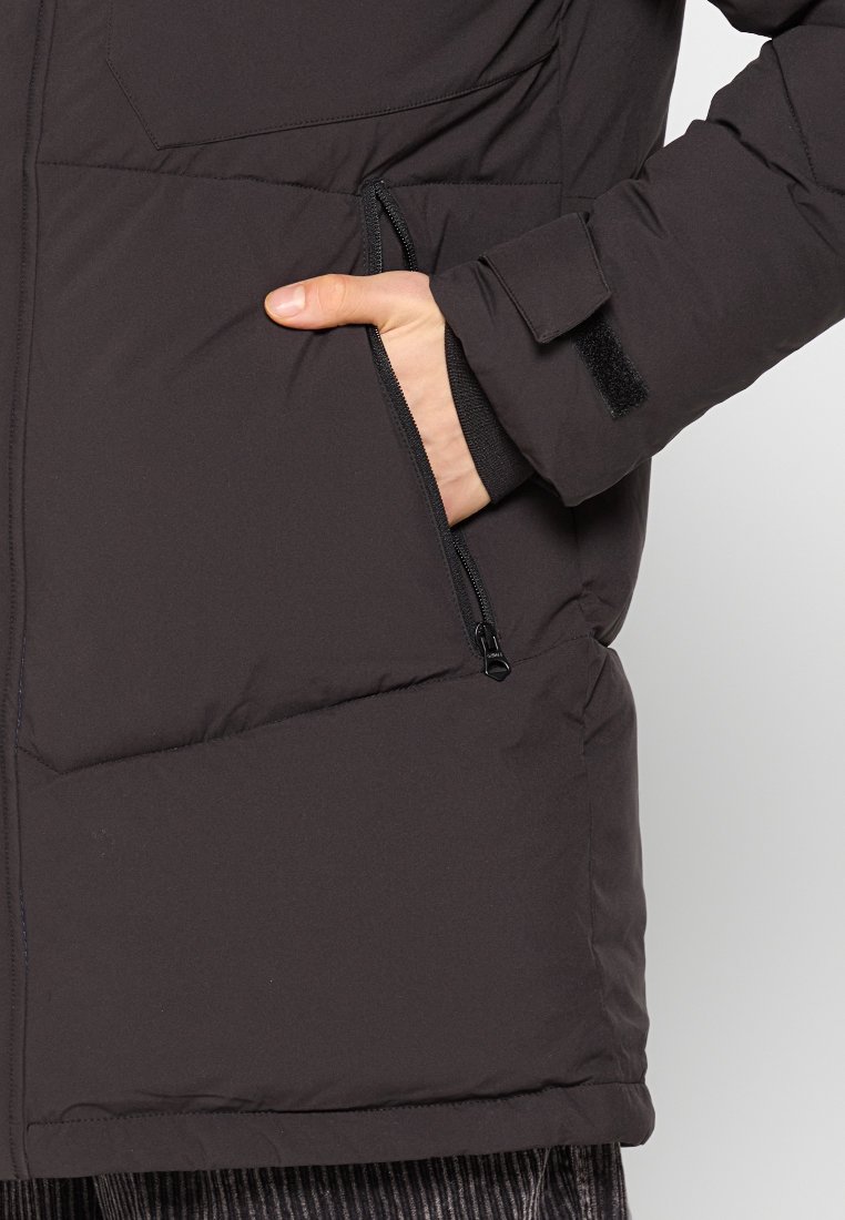 Doudoune noire avec poche zippée sur le côté et poignet en Velcro. La texture est lisse avec un design en insulation gonflée pour la chaleur.