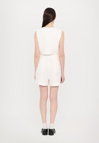 Top blanco sin mangas combinado con shorts de talle alto en color crema. La tela tiene una textura suave; los shorts cuentan con bolsillos traseros y un detalle de lazo en los lados.