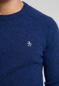Navy blue knit sweater featuring a ribbed crew neck, soft texture, and a small white penguin logo on the left chest.