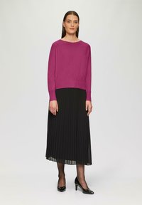 Fuchsia gebreide trui met een brede halslijn, gecombineerd met een zwarte geplooide maxi rok. De outfit wordt compleet gemaakt met zwarte hoge hakken.