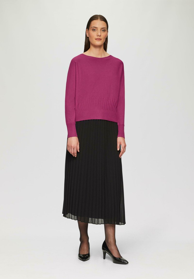 Fuchsia gebreide trui met een brede halslijn, gecombineerd met een zwarte geplooide maxi rok. De outfit wordt compleet gemaakt met zwarte hoge hakken.