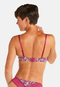 Soutien-gorge à motif floral dans des nuances de magenta et de turquoise, avec des bretelles réglables, une fermeture à crochet et une finition douce et texturée.