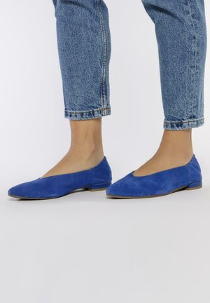 Ballerines en suede bleu avec un petit talon, présentant un bout pointu et une ouverture découpée sur les côtés. Texture lisse et design minimaliste.