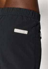 Svarte, elastiske shorts med glatt stoff, med en glidelåslomme og en lysfarget, sydd etikett med "ICEPEAK" merke.