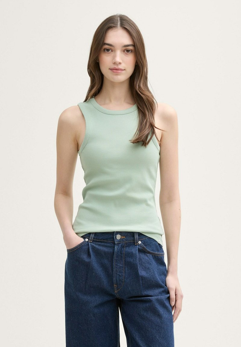 Top de tirantes acanalado verde claro con escote redondo y diseño sin mangas, combinado con unos pantalones vaqueros oscuros de denim sueltos.