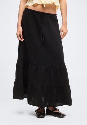 Naine kannab pikka musta kihilist seelikut, millel on seotud vöö, kombineeritud mustade lakknahast paeltega kingadega.