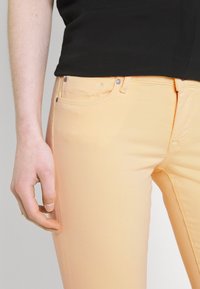 Světle broskvové džíny vyrobené z elastického materiálu, se slim fit střihem, předními kapsami, stříbrnými kovovými prvky a viditeln�ým šitím podél švů.