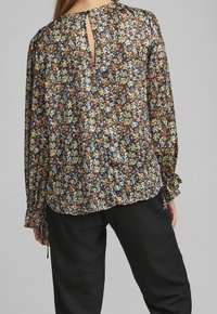 Blusa floreale con maniche lunghe, fondo nero, piccoli fiori multicolori, design a chiave sulla schiena, tessuto testurizzato, polsini elasticizzati.