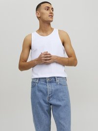 Un débardeur en coton blanc avec un col rond, porté avec un jeans en denim bleu clair. Le tissu semble doux avec une coupe décontractée.