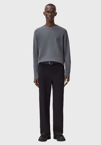 Szary sweter z okrągłym dekoltem, z subtelnym logo. W zestawieniu z czarnymi spodniami i czarnymi butami, całość o luźnym kroju i minimalistycznym designie.