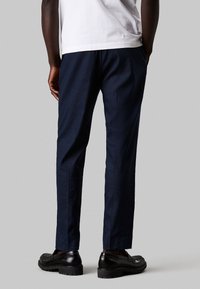 Pantaloni navy con una texture liscia, slim fit e lunghezza cropped, abbinati a mocassini neri. Il dettaglio della vita non è visibile nella vista.