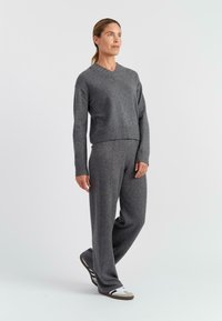 Grijze, gestructureerde gebreide trui met een V-hals en een cropped ontwerp, gecombineerd met bijpassende grijze wijde broek. Voert een minimalistisch schoeisel.
