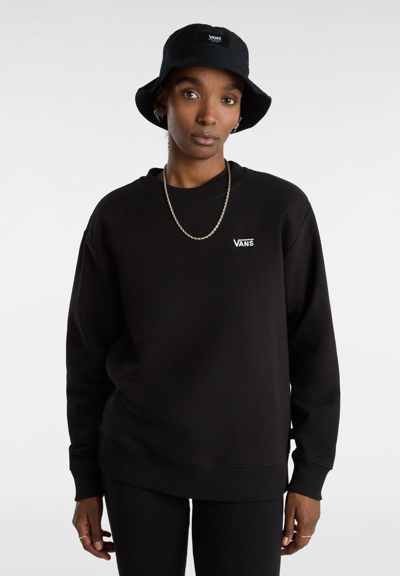 Zwarte sweatshirt met een ronde hals en geribbelde boorden, met een witte Vans-logo op de borst. Gecombineerd met een zwarte bucket hat.