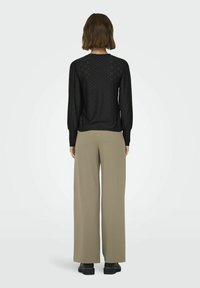 Maglione nero con motivo testurizzato e maniche lunghe, abbinato a pantaloni beige a vita alta e gamba larga, accompagnati da calzature nere.