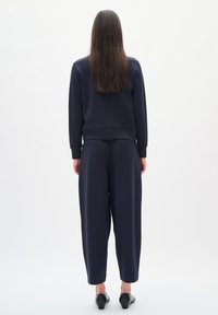 Felpa blu navy e pantaloni abbinati a vestibilità morbida, realizzati in tessuto soffice, con vita alta e polsini a coste, abbinati a scarpe nere.