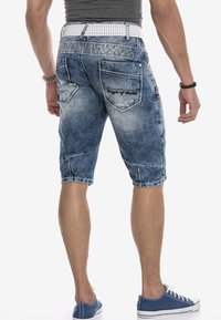 Denim shorts in verschillende blauwtinten met een vervaagde textuur, vijf zakken en decoratieve stiksels. Gecombineerd met een witte geperforeerde riem.