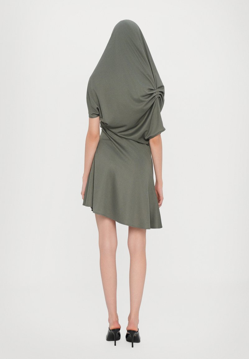 Olive green dress with a draped design, short sleeves, seamless texture, and a flared hem, viewed from the back. Black high-heeled shoes.