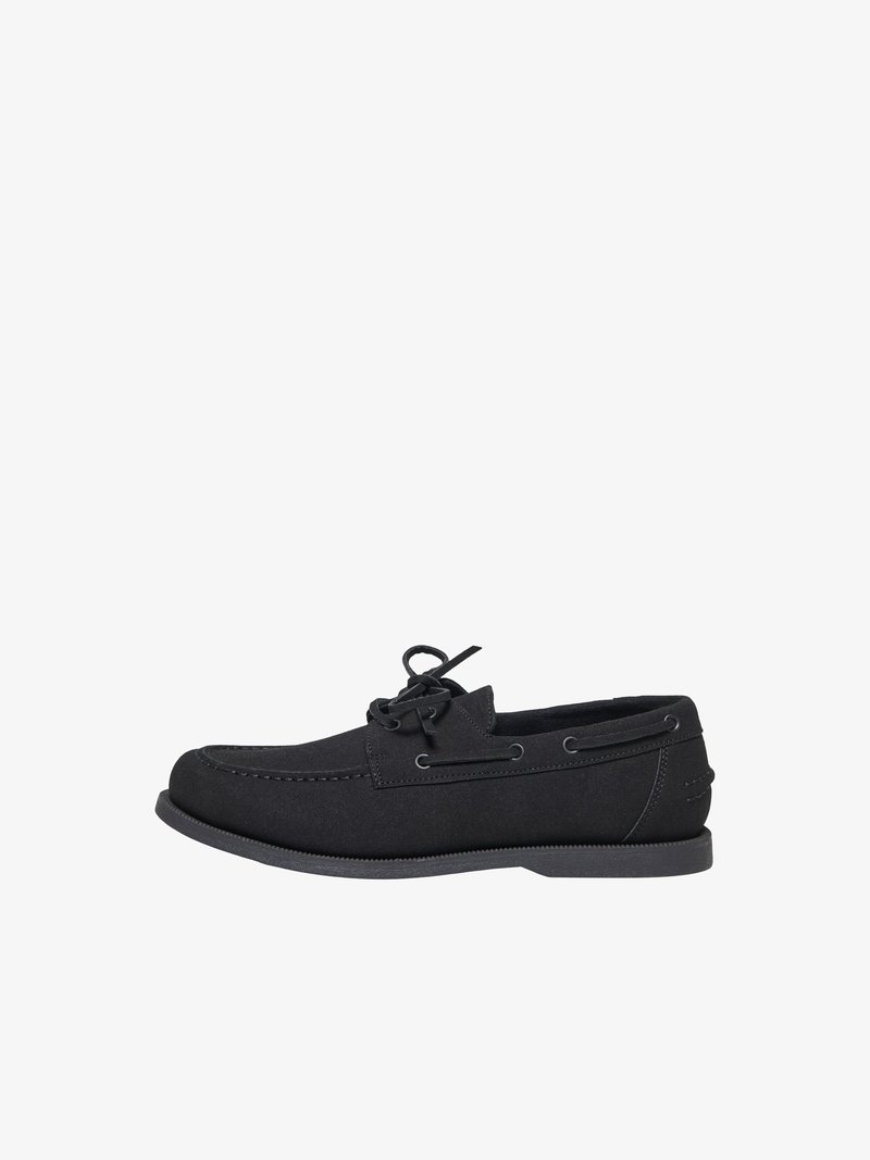 Chaussure bateau en daim noir avec laçage à l'avant, couture moc toe, et semelle basse plate, montrée de profil sur fond blanc.