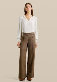 Blouse blanche avec un col en V et des cordons, assortie à un pantalon marron à carreaux houndstooth taille haute et large, accentué d'un bouton.