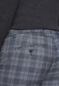 Grå och marinblå rutiga byxor med en knäppt bakficka och textil med struktur. Åtsittande design med en midjehöjd ovanför. 