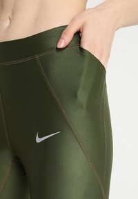 Zielone legginsy sportowe wykonane z elastycznego materiału o gładkiej fakturze, z boczną kieszenią i małym białym logo Nike.