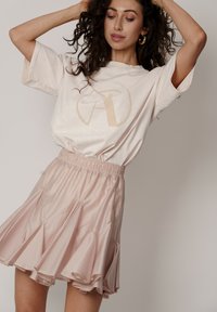Kremowy oversize t-shirt z beżowym logo; zestawiony z jasnoróżową rozkloszowaną spódnicą z elastycznym pasem i warstwowymi falbanami.