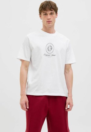Hvid bomulds t-shirt med rund halsudskæring, korte ærmer og et centralt grafisk logo i sort blæk, parret med røde bukser.