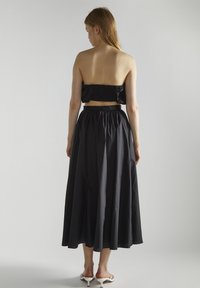 Conjunto de dos piezas negro que presenta un top bandeau con fruncido y una falda larga y fluida. La tela parece ligera con una textura ligeramente brillante.