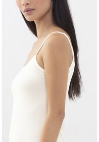 Camisola color crema con spalline sottili regolabili, trama liscia e silhouette aderente, mostrata su uno sfondo neutro.