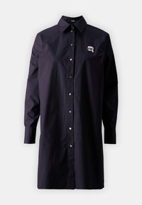 Schwarzes Hemd mit Knöpfen aus leichtem Stoff, mit langen Ärmeln, klassischem Kragen und einem kleinen bestickten Muster auf der Brust.