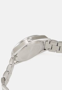 Reloj de acero inoxidable plateado con una caja suave, cara redonda y pulsera de eslabones metálicos. Presenta una corona prominente y un diseño minimalista.