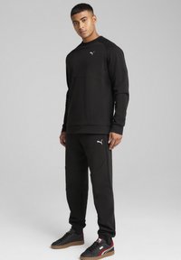 Svart atletisk sweatshirt och träningbyxor i mjukt material, med en subtil logo, strukturerad design och tapered passform, tillsammans med svarta sneakers.