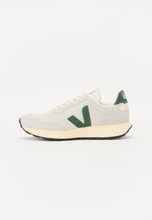 Lichtgrijze sneaker met een gestructureerde afwerking, groene suède logo, crème zool en zwarte rubberen loopzool; voorzien van een vetersluiting.