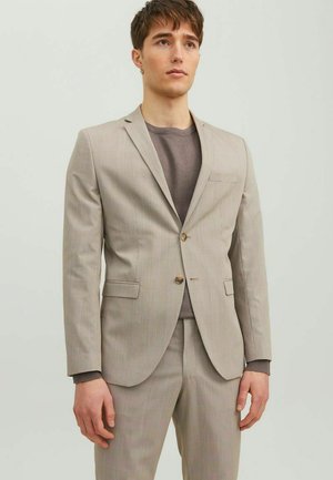 Beige pinstriped suit with a two-button blazer, notched lapels, and matching trousers. Worn over a gray crew-neck shirt.