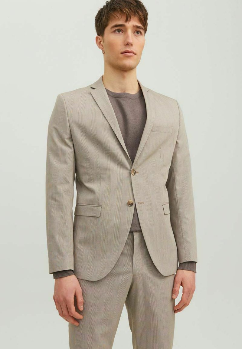Completo beige a righe con giacca a due bottoni, colletto a punta e pantaloni abbinati. Indossato su una maglietta grigia girocollo.
