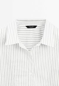 Camicia bianca con sottili righe verticali nere e un unico bottone bianco visibile, etichettata "Massimo Dutti, Made in Portugal."